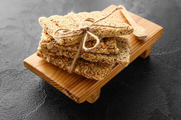 Wooden board with stack of tasty sesame kozinaki bars on dark background