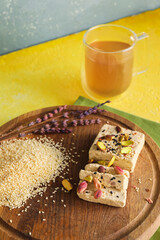 Wooden board of tasty sesame halva with pistachios on color table, closeup