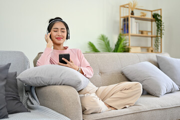 Chilling and relaxing Asian female on sofa, listening to music through her headphones.