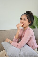 Fototapeta premium Attractive Asian female eating yummy doughnuts while relaxing in her living room.