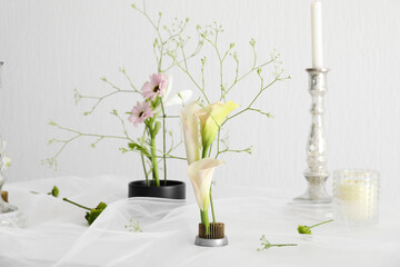 Beautiful ikebanas and candles on table near white wall