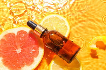 Bottle of citrus serum with fruits in water on color background, closeup