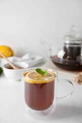 Glass cup of black tea with lemon and mint on white table, closeup