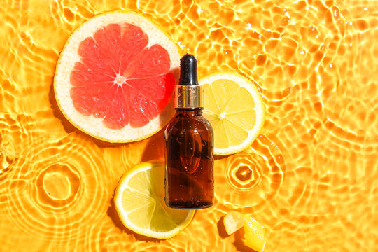 Bottle of citrus serum with fruits in water on color background
