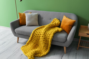 Grey sofa with cushions and yellow plaid near green wall