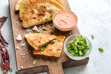 Wooden board with tasty chebureks, sauce and green onion on light background, closeup