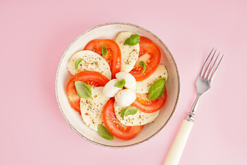 Bowl of tasty caprese salad on pink background