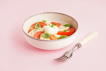 Bowl of tasty caprese salad on pink background