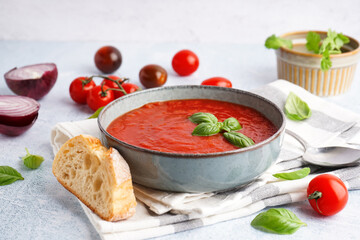 Bowl of tasty tomato soup and bread on light background