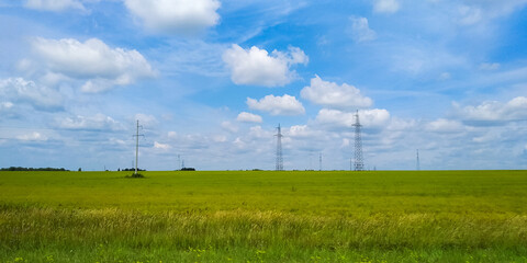 Beautiful cloudy landscape over a field with green grass and power lines