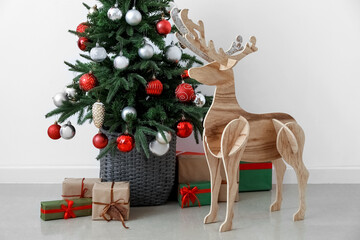 Wooden reindeer with Christmas tree and presents near light wall