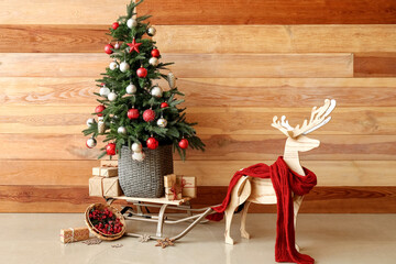 Decorative reindeer with scarf, sledge, Christmas tree and presents near wooden wall