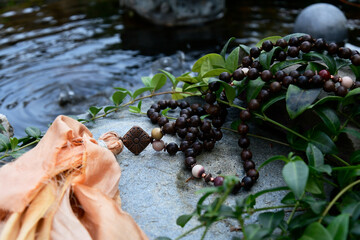 An image of mala meditation beads resting on a flat rock at the edge of a bubbling water pond.