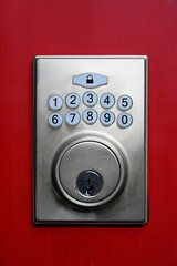 A close up image of a digital key pad on a red painted exterior door. 