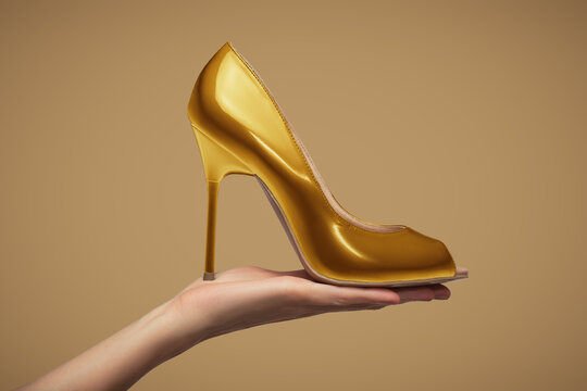 Female hand holding a gold-colored high-heeled shoe.