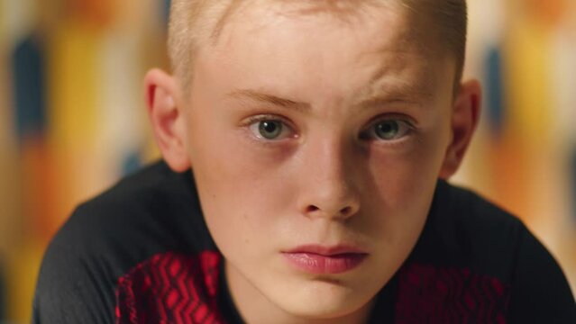 Blonde teenage boy face closeup portrait. Looks at the camera and fixes his hair. Closeup footage of a young teen boy. Adolescent anxiety, emotional.
