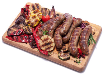 Grilled sausages and vegetables on wooden cutting board isolated on white background