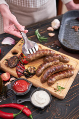 Grilled sausages and vegetables on wooden cutting board at domestic kitchen