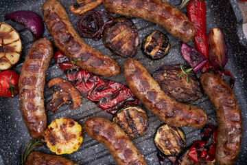 Fototapeta premium Grilled sausages and vegetables on a grill frying pan on a domestic kitchen