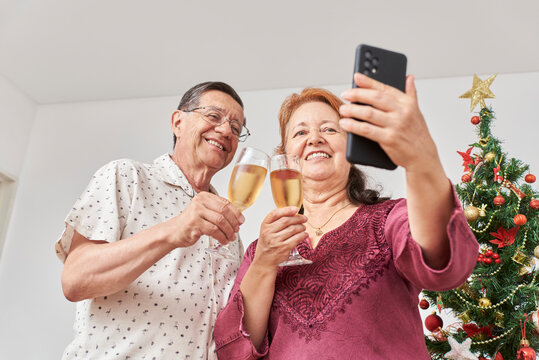 Happy senior latin couple talking by video call while toasting during Christmas or New Year, celebrating holidays at home, together. Low angle view composition with copy space.