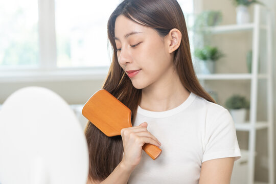 Health hair care, beauty makeup asian woman, girl holding hairbrush and brushing, combing her long straight hair looking at reflection in mirror in morning routine after salon treatment, hairstyle.