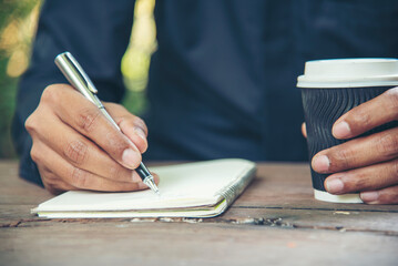 Man hands writing notebook diary with coffee cup and smartphone on wood desk. Close up man hands...