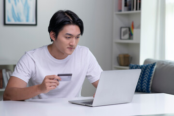 Young Asian man holding credit card and using laptop computer. Businessman working at home. Online shopping, e-commerce, internet banking, spending money, working from home concept