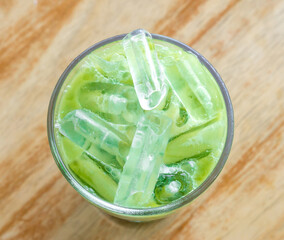 Top view of iced matcha latte or condensed milk-added green tea in transparent glass on blurred brown wood background