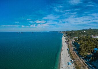 long Black Sea pebble beach with clear water on a windless sunny summer morning - aerial drone view of the horizon towards the city of Tuapse