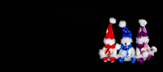 Banner with three handmade toy snowmen with hats and scarves on a black background. Christmas and New Year concept