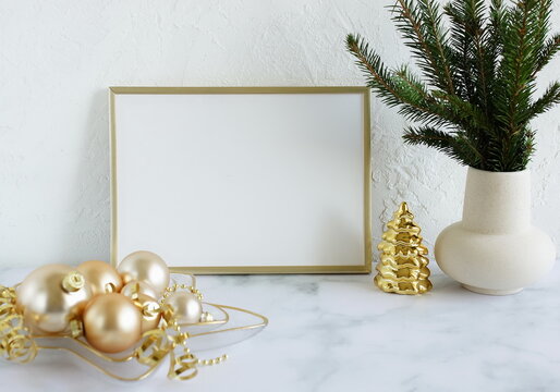 Christmas interior composition with   frame mockup,Xmas Tree branches in a vase and golden christmas decorations. White wall and marble table  background. Copy space. 