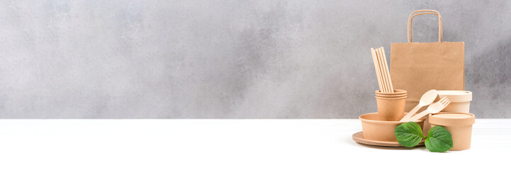 Various paper utensils - food paper containers, bag, cups, drinking straws and wooden cutlery set against gray wall background with copy space. Sustainable food packaging. Banner