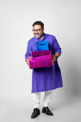 Young happy Indian man holding gift box and wearing traditional cloths, standing against white background