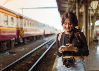 Fototapeta na wymiar back view of woman wearing black long sleeve t-shirt carrying backpack on shouder holding cellphone standing in railway station,travel concept,social network technology concept