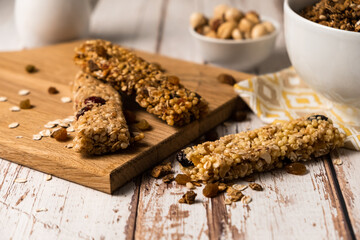 Various energy bars with granola chocolate in a row with scattered nuts, cereals and dried fruits, a grunge background of a white wood table. A healthy vegan snack for fitness. Close-up.