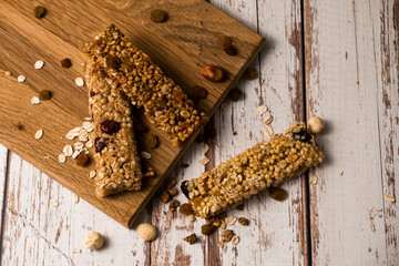 Various energy bars with granola chocolate in a row with scattered nuts, cereals and dried fruits, a grunge background of a white wood table. A healthy vegan snack for fitness. Close-up.