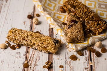 Various energy bars with granola chocolate in a row with scattered nuts, cereals and dried fruits, a grunge background of a white wood table. A healthy vegan snack for fitness. Close-up.