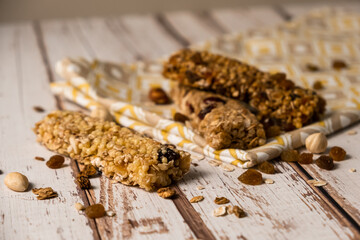 Various energy bars with granola chocolate in a row with scattered nuts, cereals and dried fruits, a grunge background of a white wood table. A healthy vegan snack for fitness. Close-up.