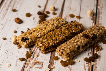Various energy bars with granola chocolate in a row with scattered nuts, cereals and dried fruits, a grunge background of a white wood table. A healthy vegan snack for fitness. Close-up.