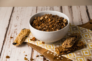 Energy breakfast. Chocolate granola with dried fruits in a bowl, various granola bars on a light wooden background.