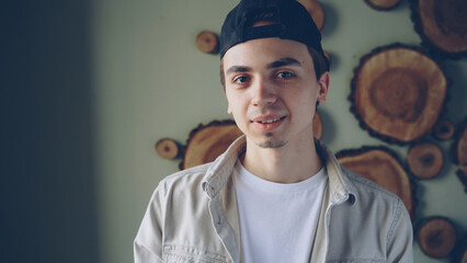 Close-up portrait of handsome young man wearing black cap, white T-shirt and trendy beige shirt looking at camera and smiling. Attractive people and fashion concept.