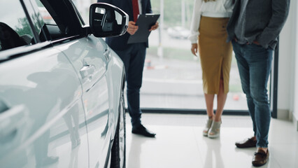 Low shot of prosperous people young couple buying new car in dealership and talking to helpful...