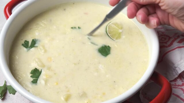 Mexican corn soup with cheese and herbs in a red saucepan. Vegan recipe concept.