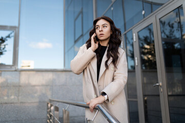 stylish businesswoman talking on a mobile phone at the entrance to the office center