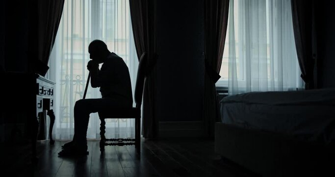 Silhouette of old man sitting in his bedroom alone feeling lonely, loneliness concept.