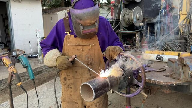 Close-up shot of an experienced welder welding a pipe outside