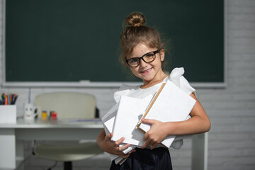 Cute little school kid girl with books in a classroom. Elementary school and primary education.