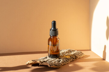 Serum in amber-colored glass bottle with dropper lid on stand made of piece of tree bark. Essential...