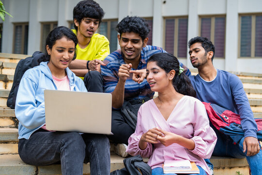 Group of happy students checking results on laptop while sitting on college campus - concept of education, technology and project work discussion.