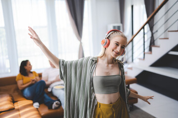 Happy young girl uses headphones to listen to music while relaxing at home with her family, and a gorgeous smiley woman enjoys her pastime and leisure time in the entertainment room.